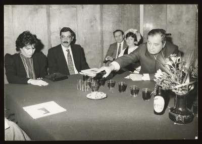 Czarno-białe zdjęcie. Sześciu mężczyzn i kobieta stojąca w środku stoją na półpiętrze wewnętrznych schodów Zachęty. W tle detale architektoniczne.